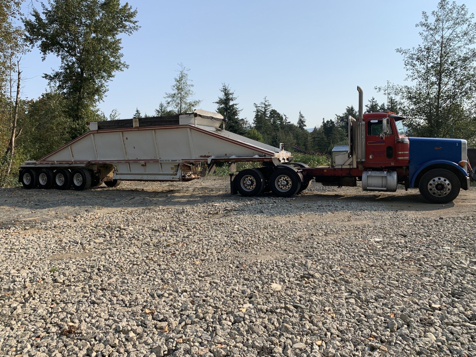 A red semi truck is pulling a white trailer on a gravel road