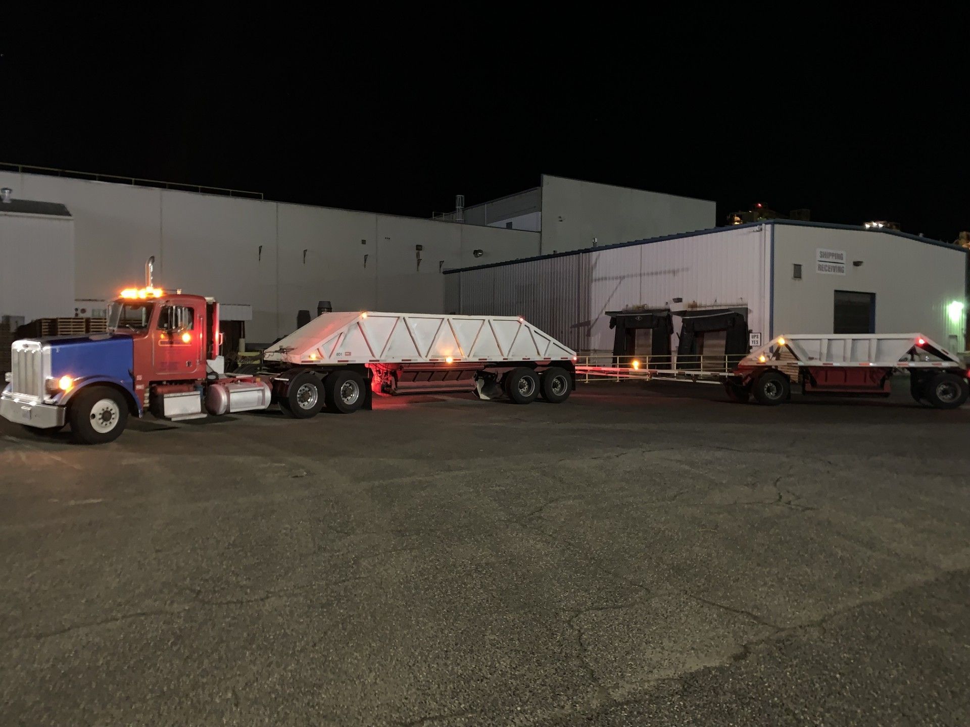 Two semi trucks are parked in front of a building at night.