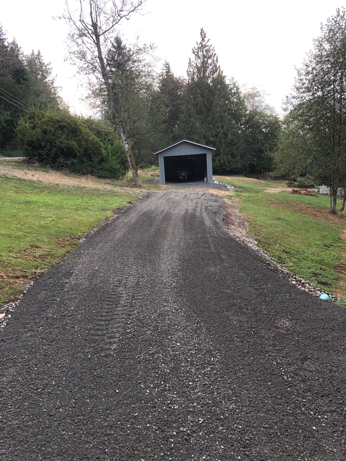 A gravel driveway leading to a garage in the middle of a grassy field.