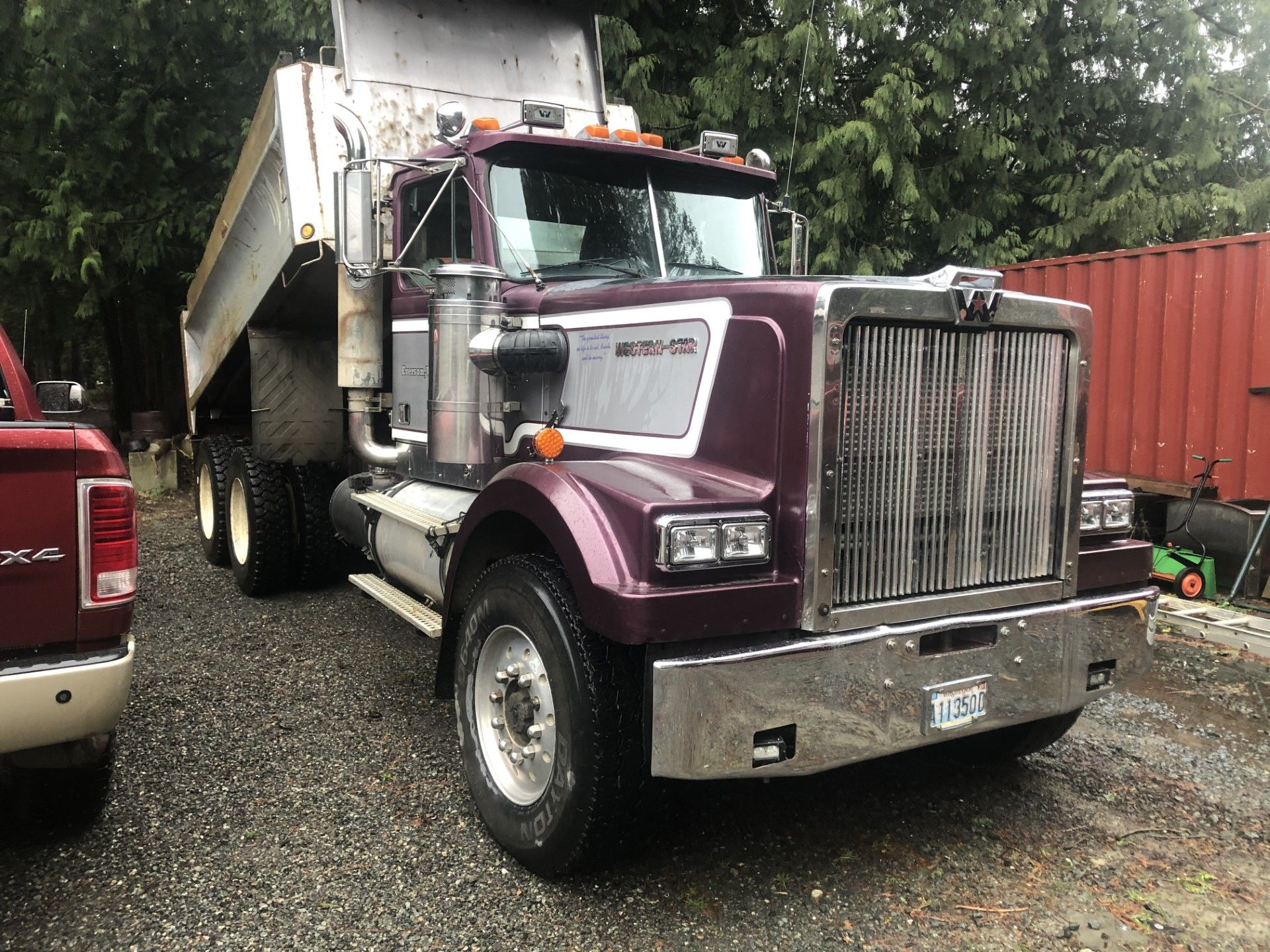 A purple dump truck is parked in a gravel lot next to a red truck.