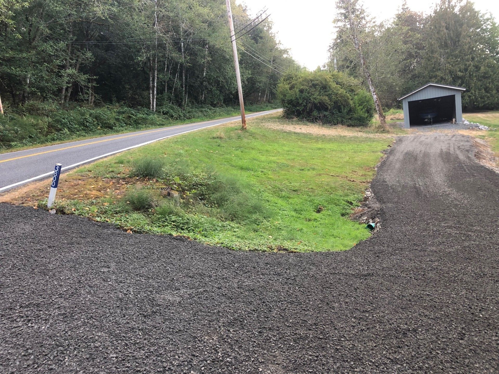 A gravel driveway leading to a garage next to a road.