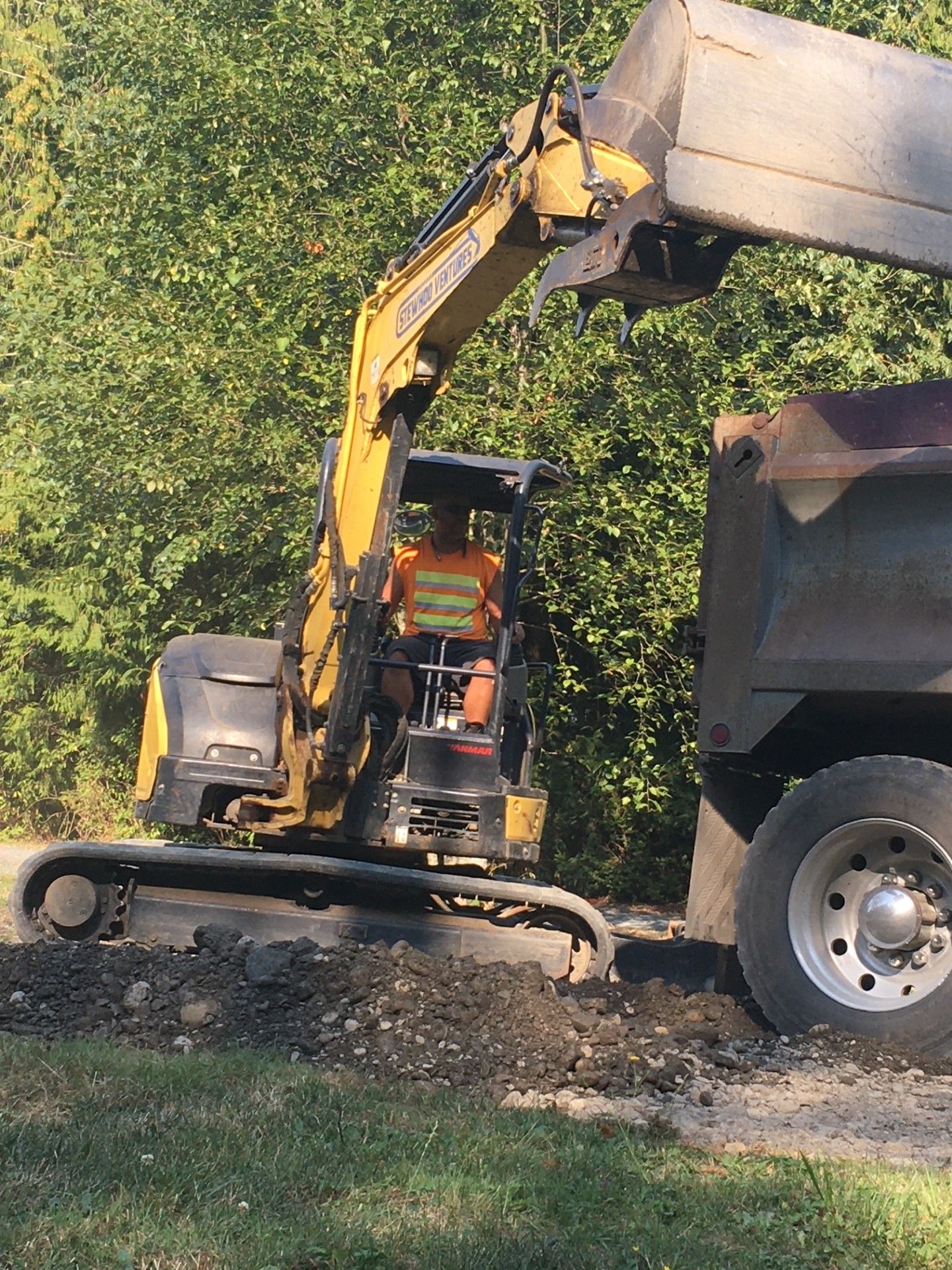 A man is driving an excavator next to a dump truck.