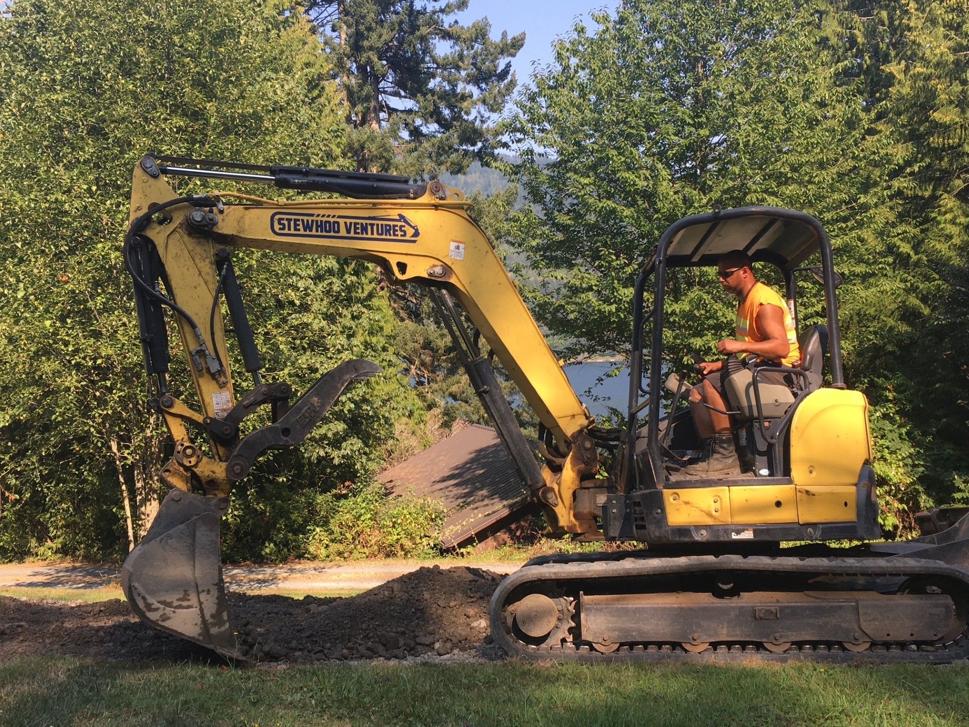 A man is driving a yellow excavator in a yard.