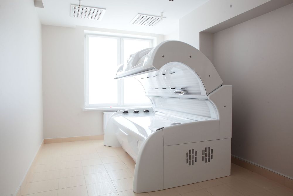 A white, enclosed hydrotherapy bed in a light-colored room. Sunlight shines through a window.