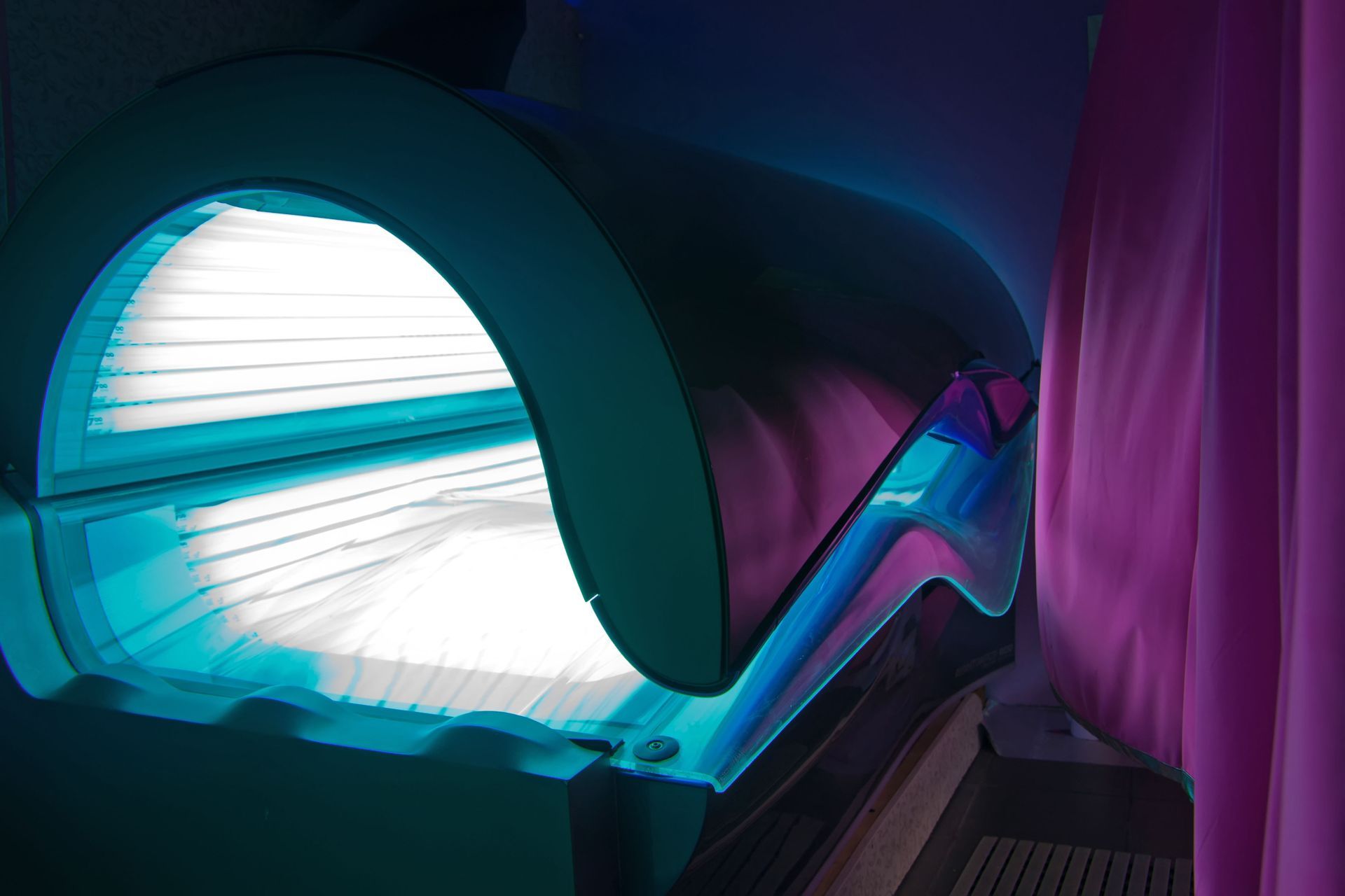 Tanning bed with bright blue lights, inside a room with a pink curtain.