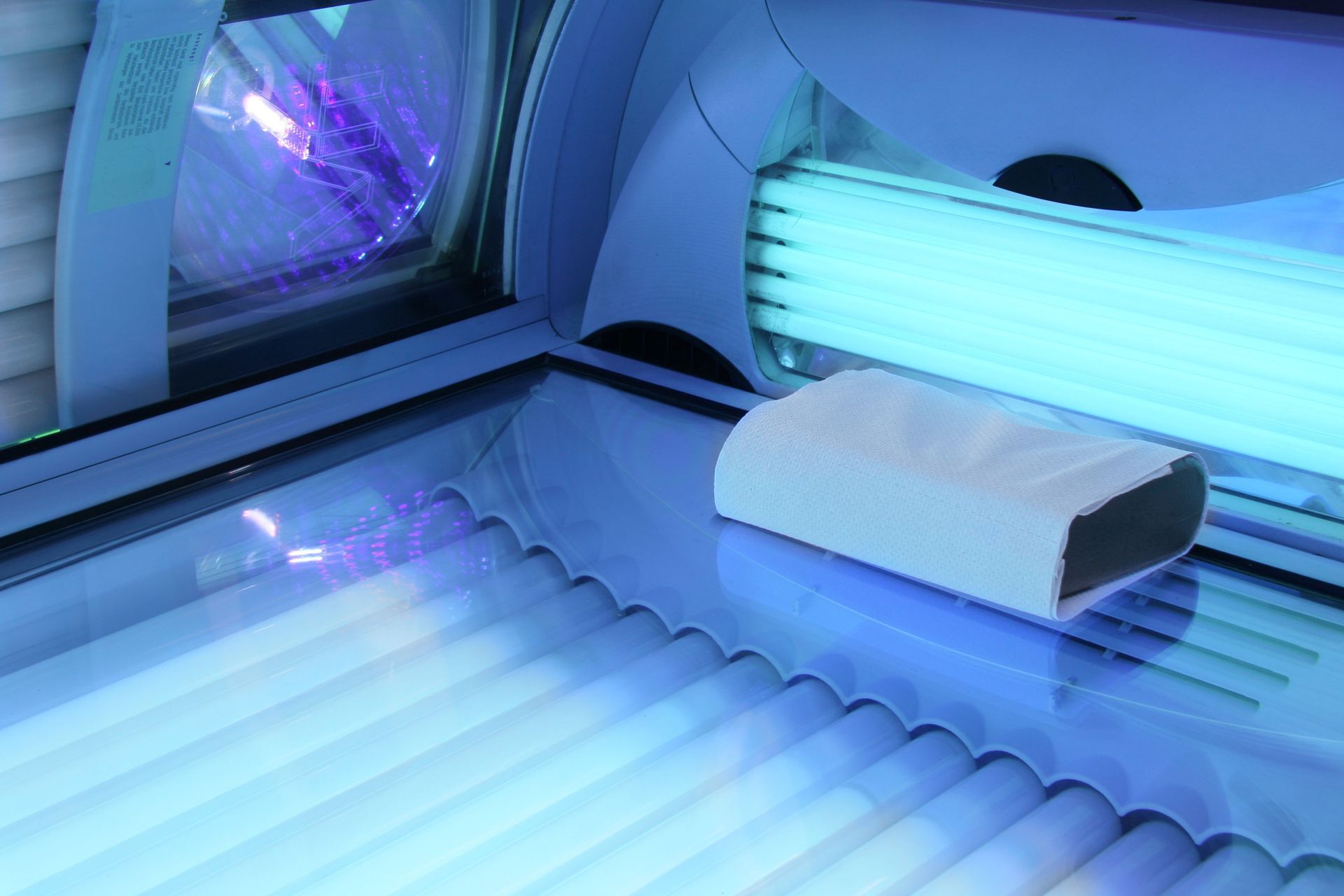 Tanning bed interior with glowing blue UV lights and a white headrest.