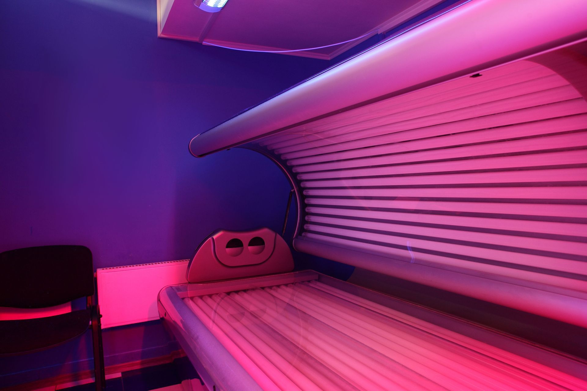 Tanning bed in a purple-lit room, with a chair in the corner.