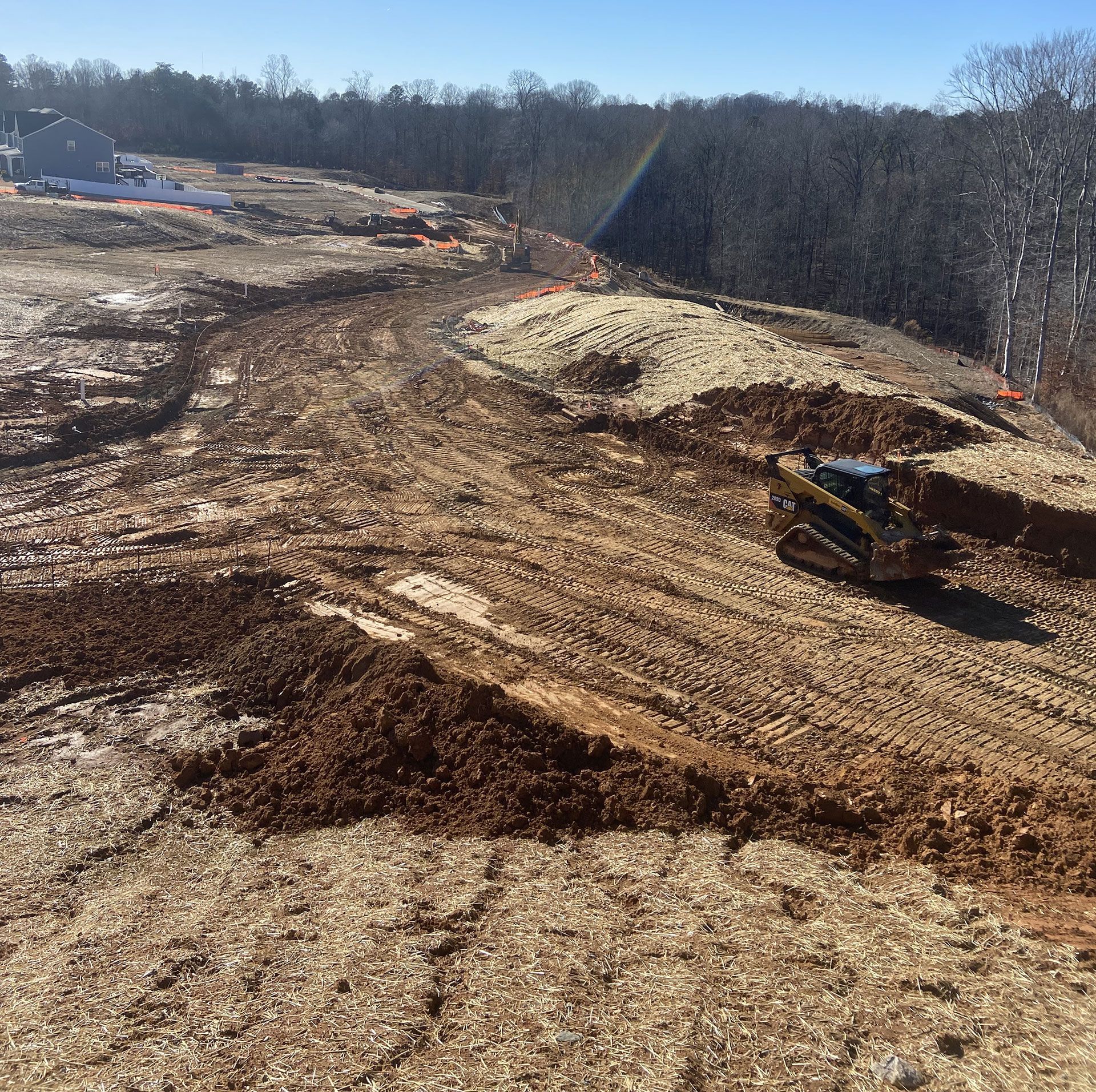 Construction site with excavator grading a dirt hillside beside a wooded area