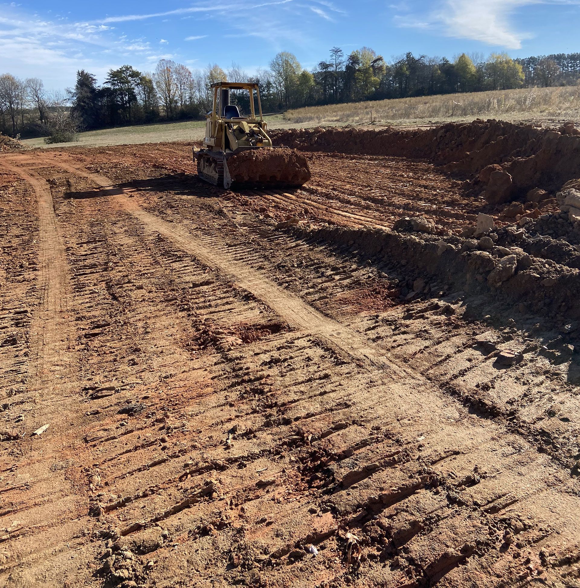 Bulldozer leveling a dirt excavation site under a blue sky.