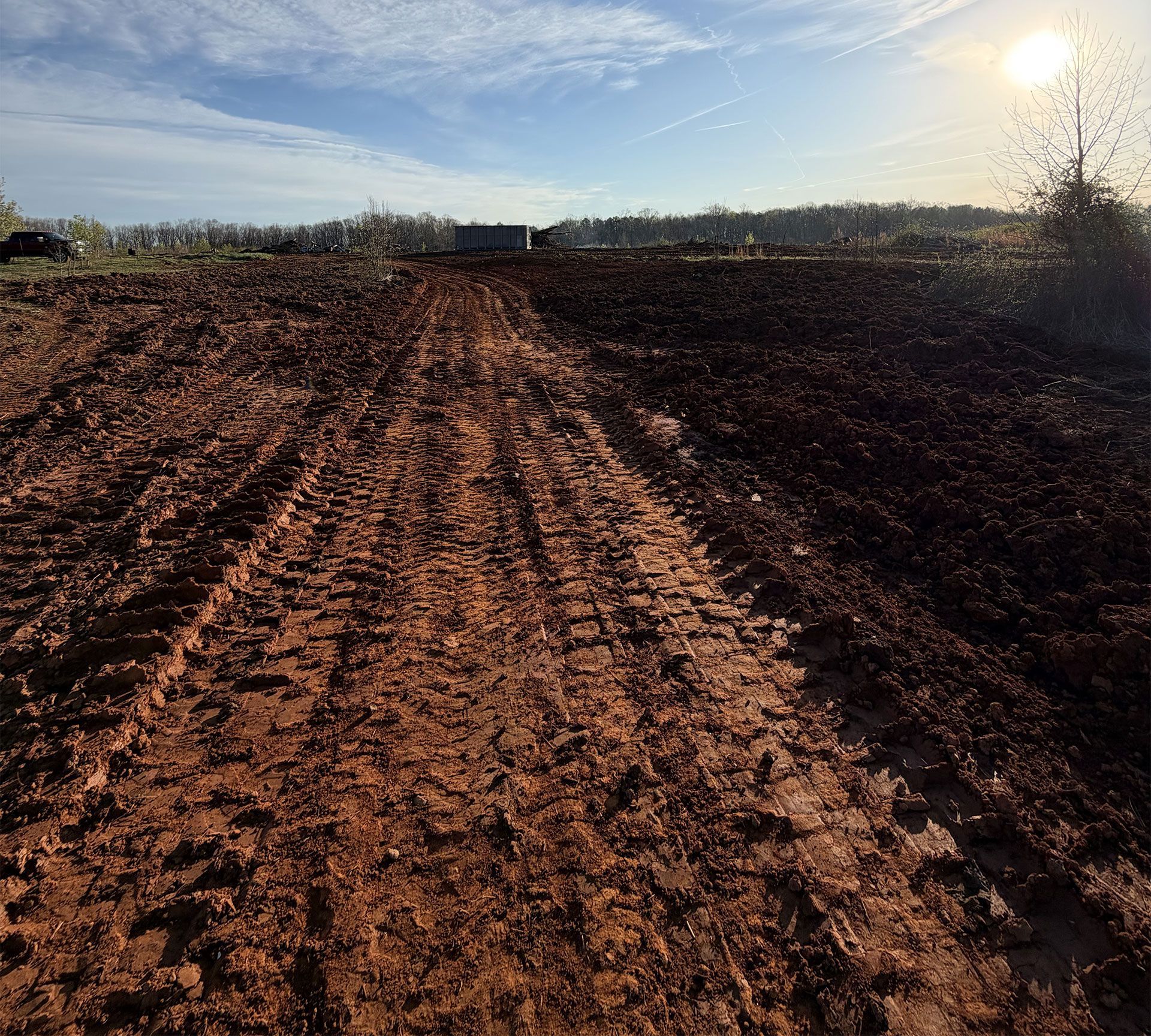 Freshly plowed red-brown field under a bright low sun, with furrows leading toward the horizon