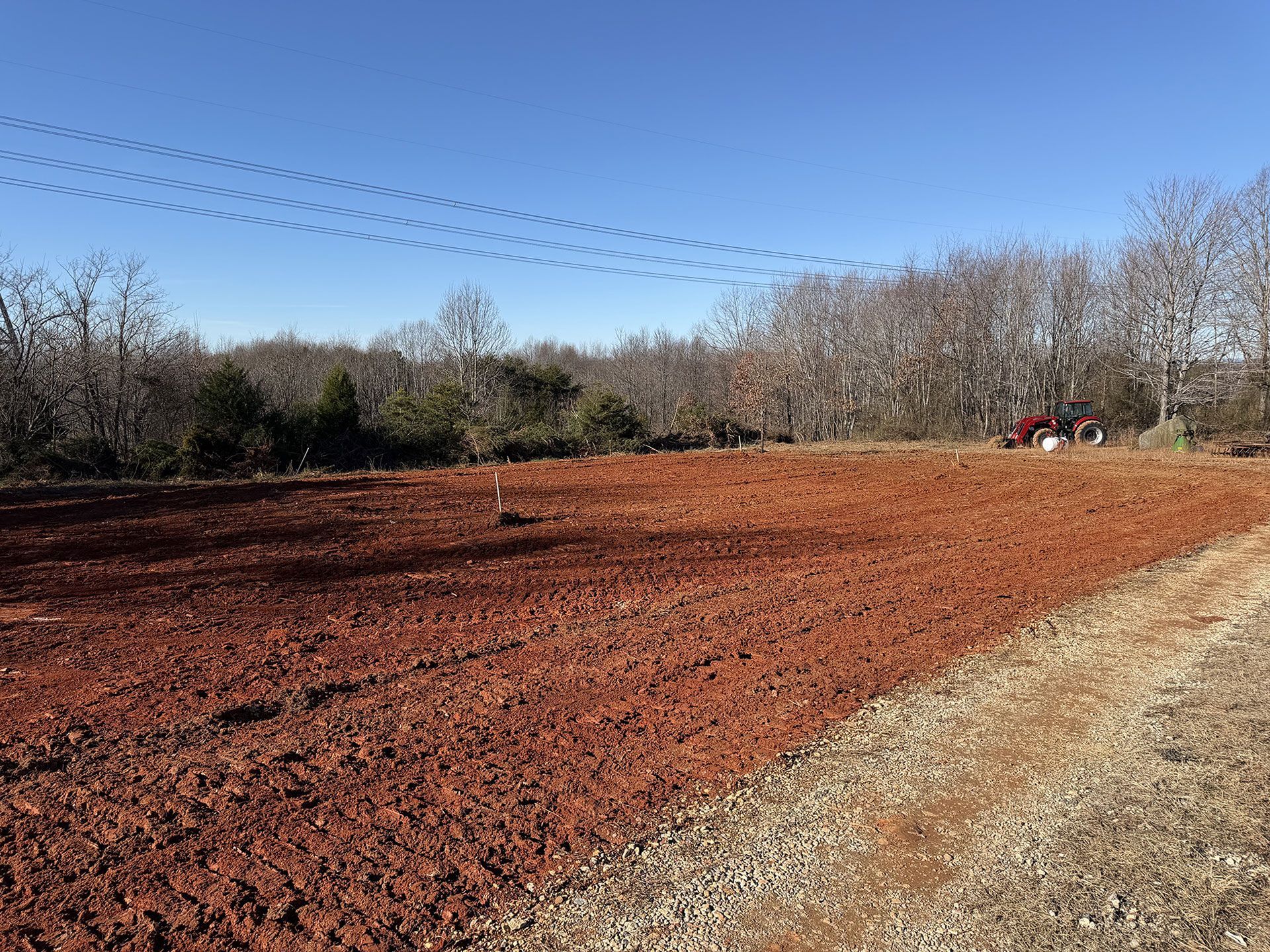Red dirt field with a gravel edge, bare trees, and a blue sky overhead