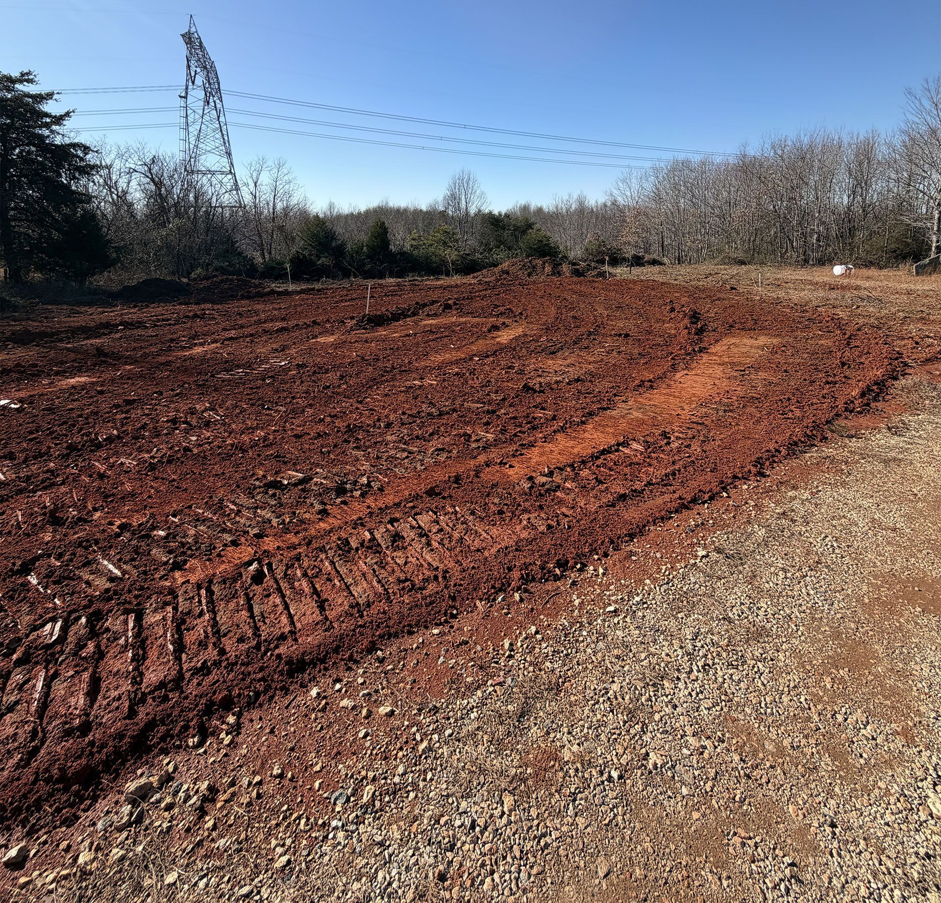 Red dirt road curving through a wooded area under a clear blue sky