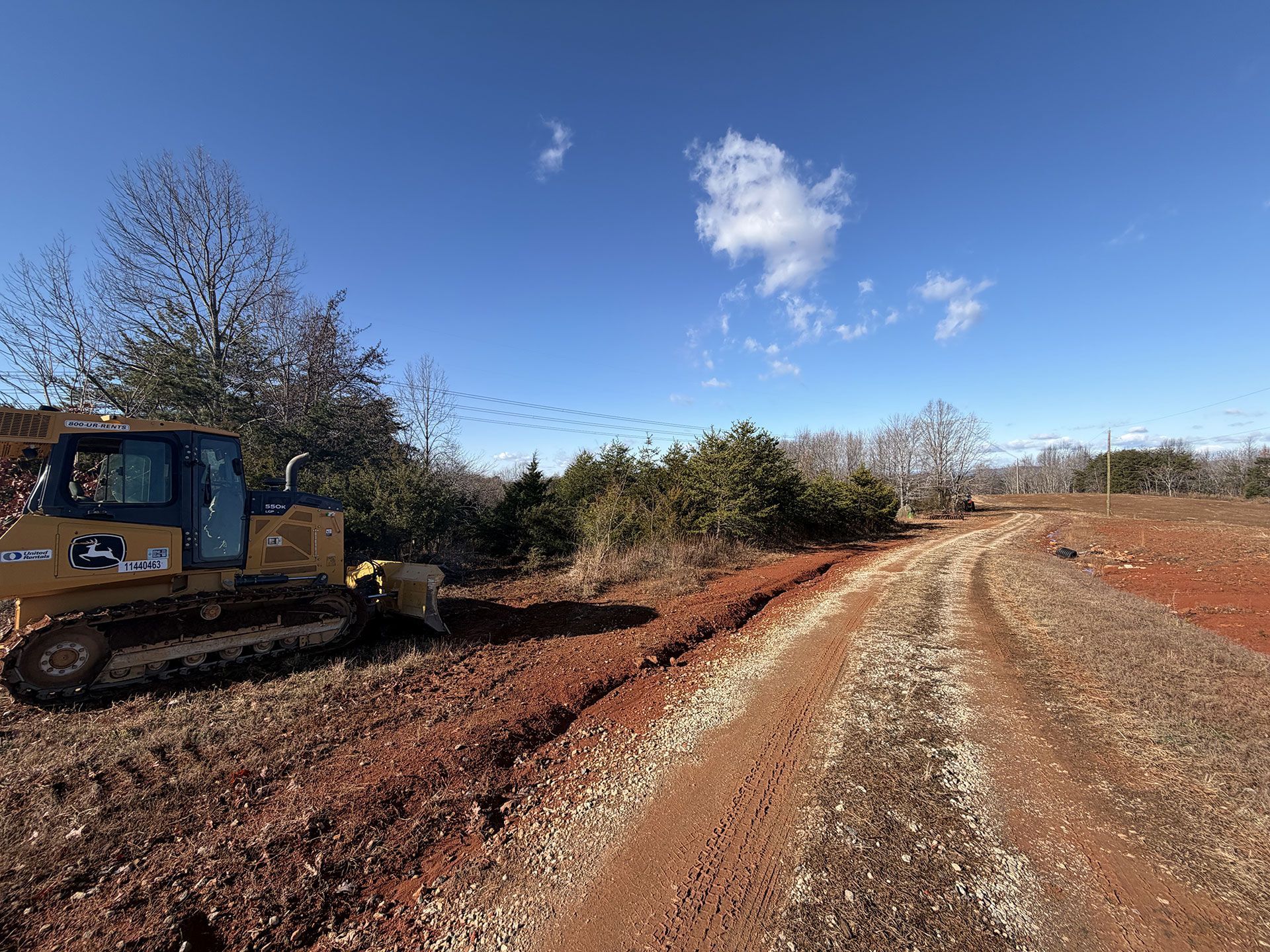 Bulldozer grading a dirt road under a blue sky with trees along the roadside