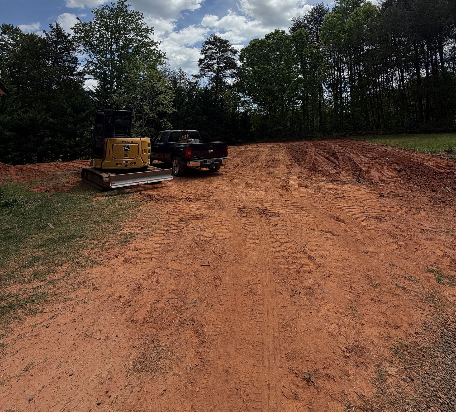 Yellow excavator and black machine on a dirt clearing surrounded by trees under a cloudy sky