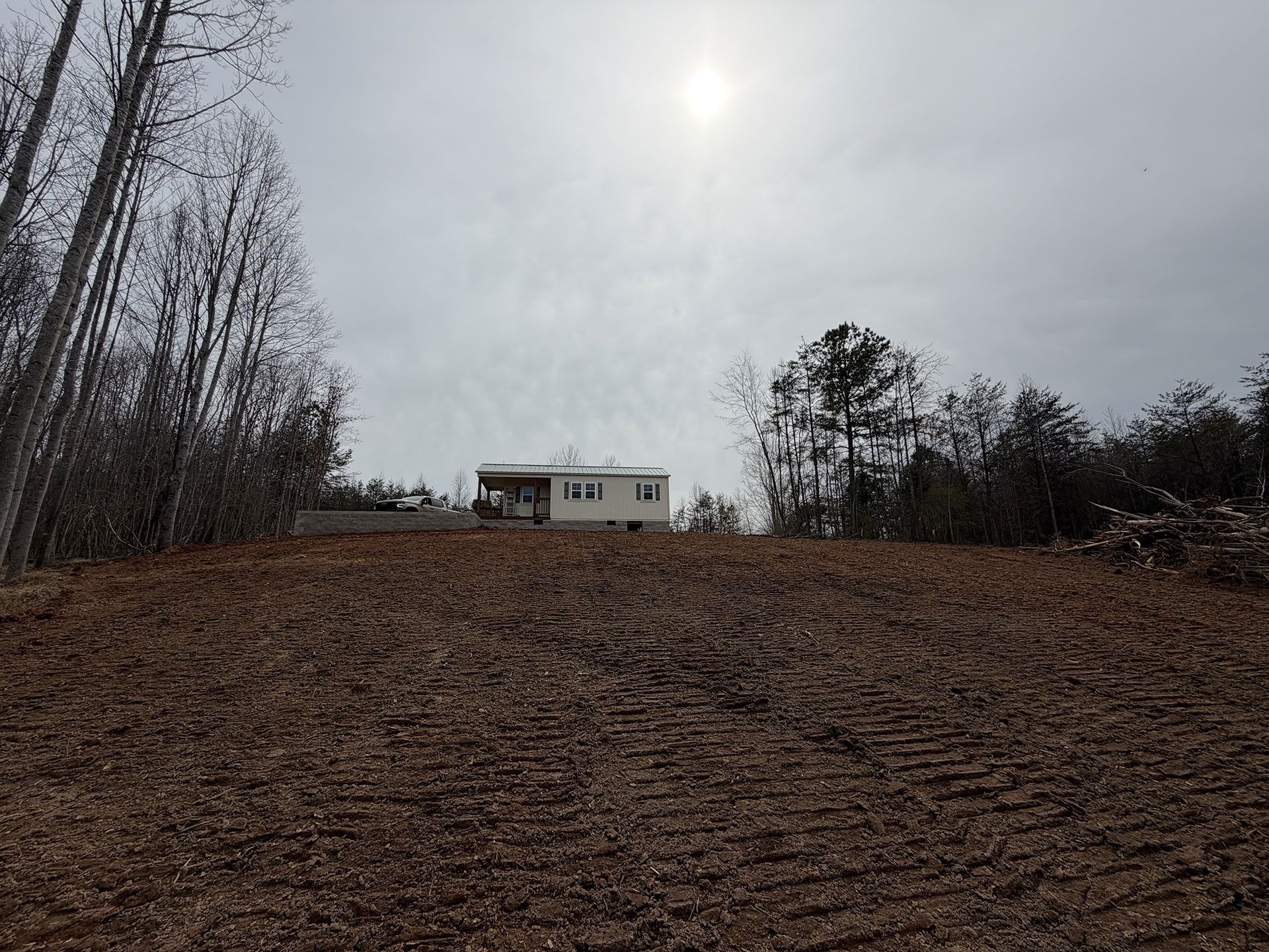 Snowy field under a cloudy sky with a small building in the distance and bare trees at the edges