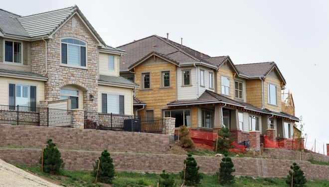 Row of newly built stone and wood townhouses on a sloped hillside with front porches and landscaping