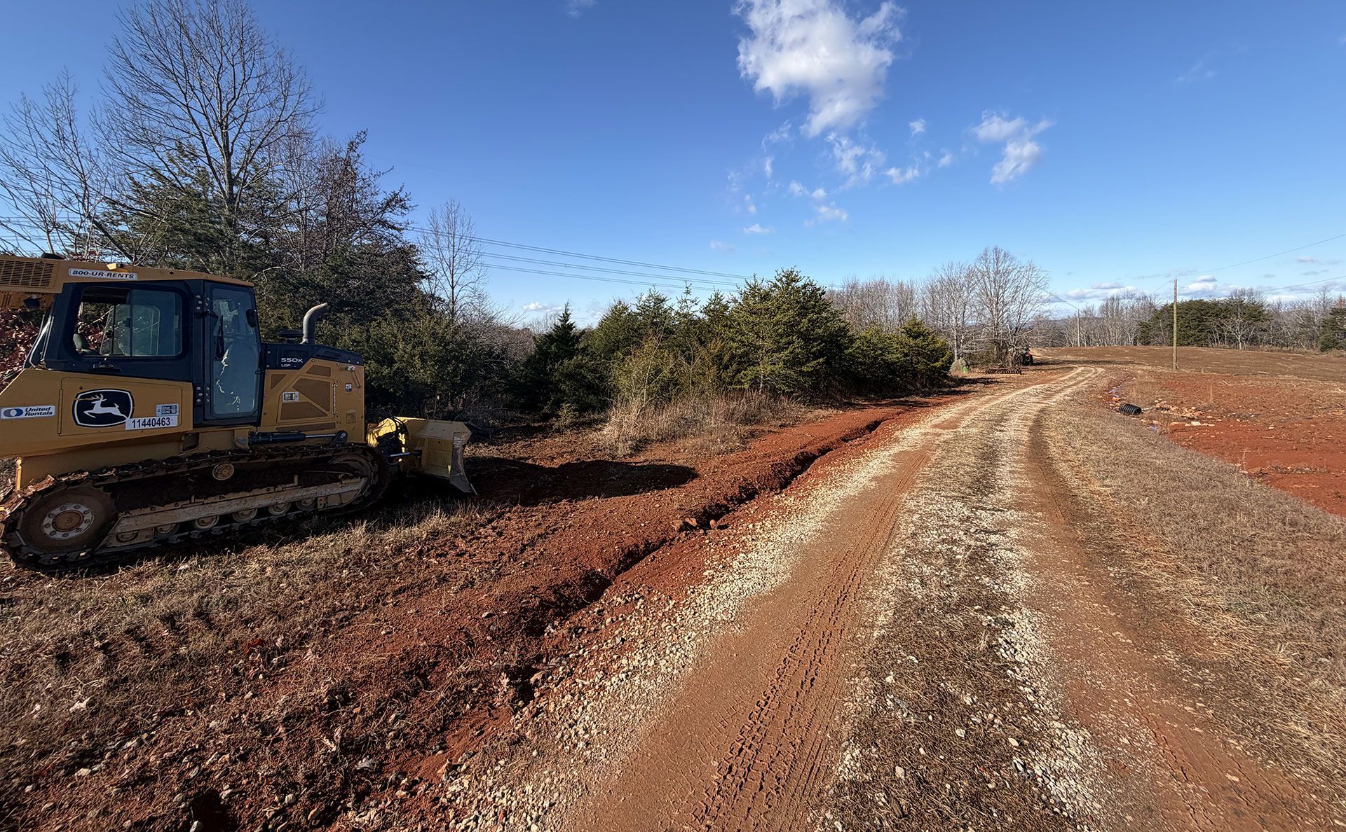 Bulldozer grading a dirt road beside a gravel path under a blue sky
