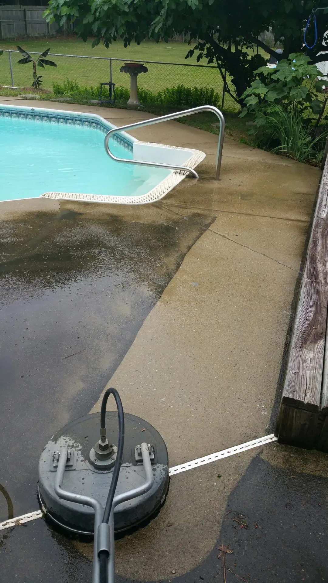 A pressure washer is sitting on the sidewalk next to a swimming pool