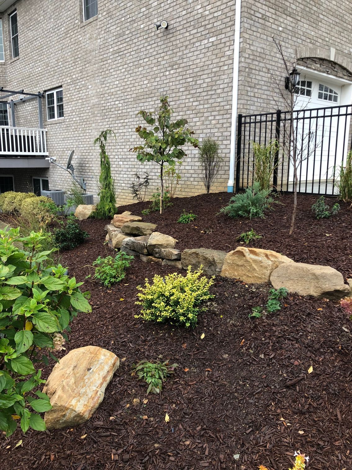 A garden with rocks and plants in front of a brick house.