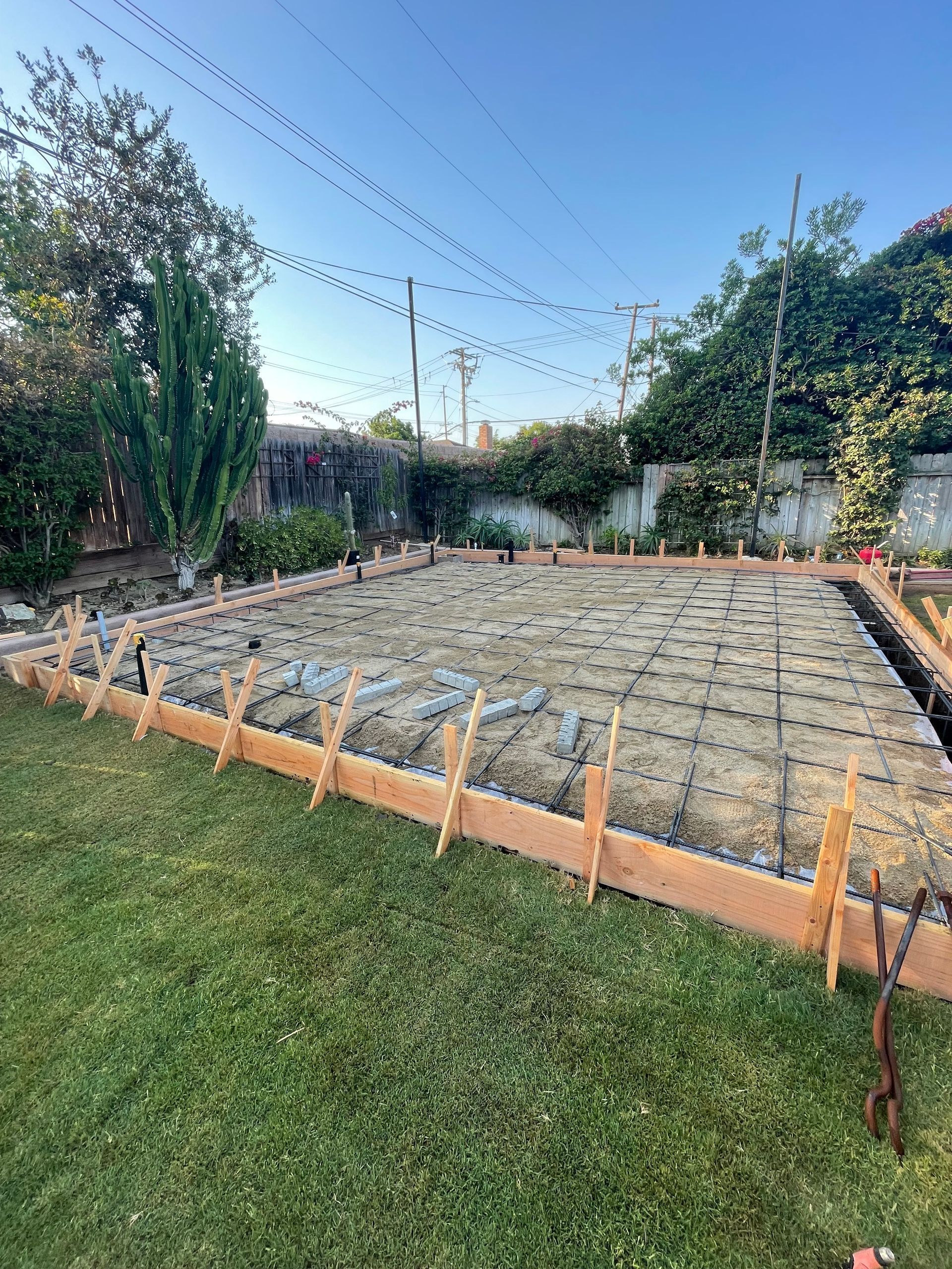 Construction site in backyard: wooden forms, rebar grid, preparation for concrete slab.