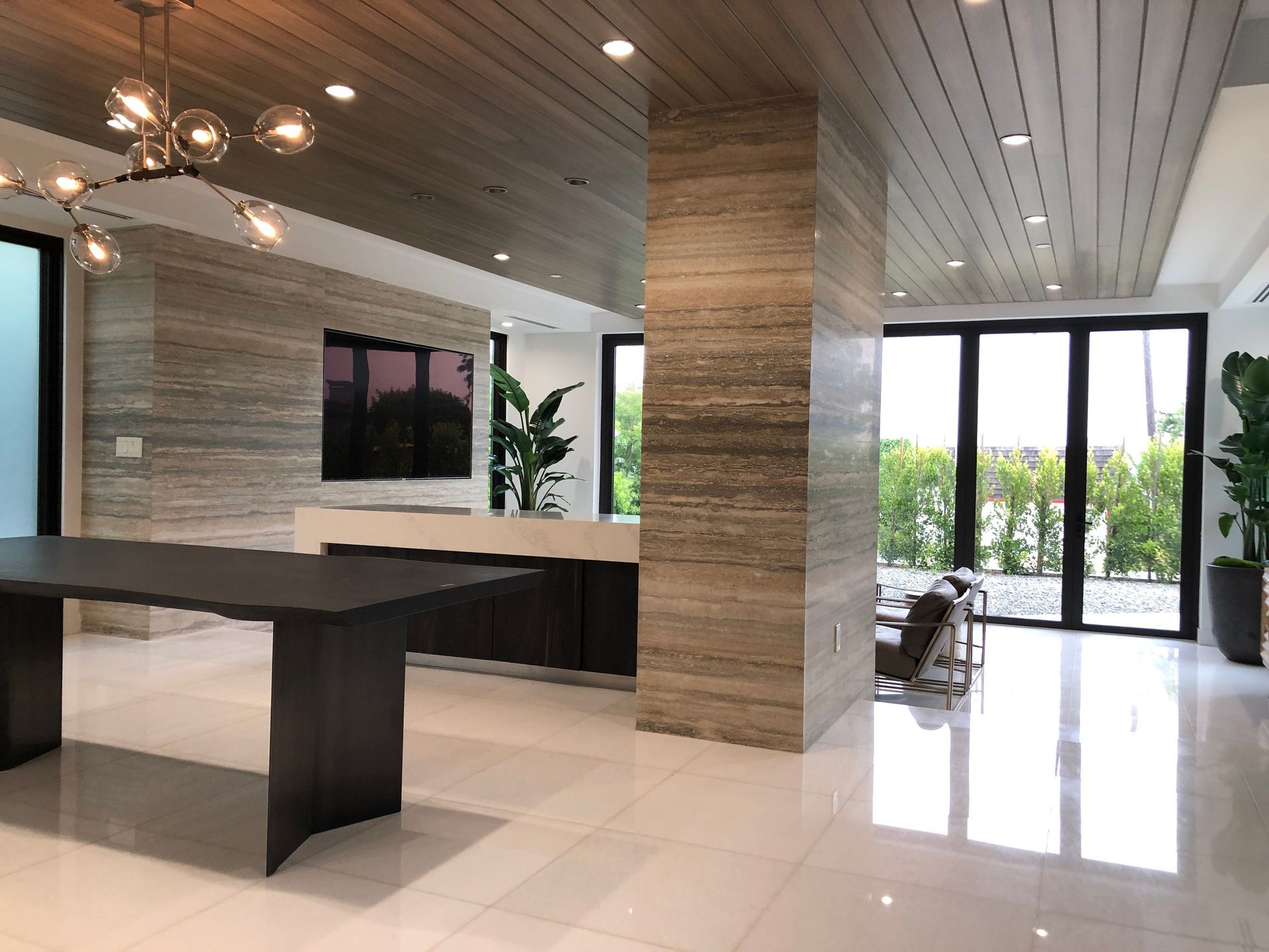 Modern interior with marble walls, wood ceiling, dark table, and large windows.