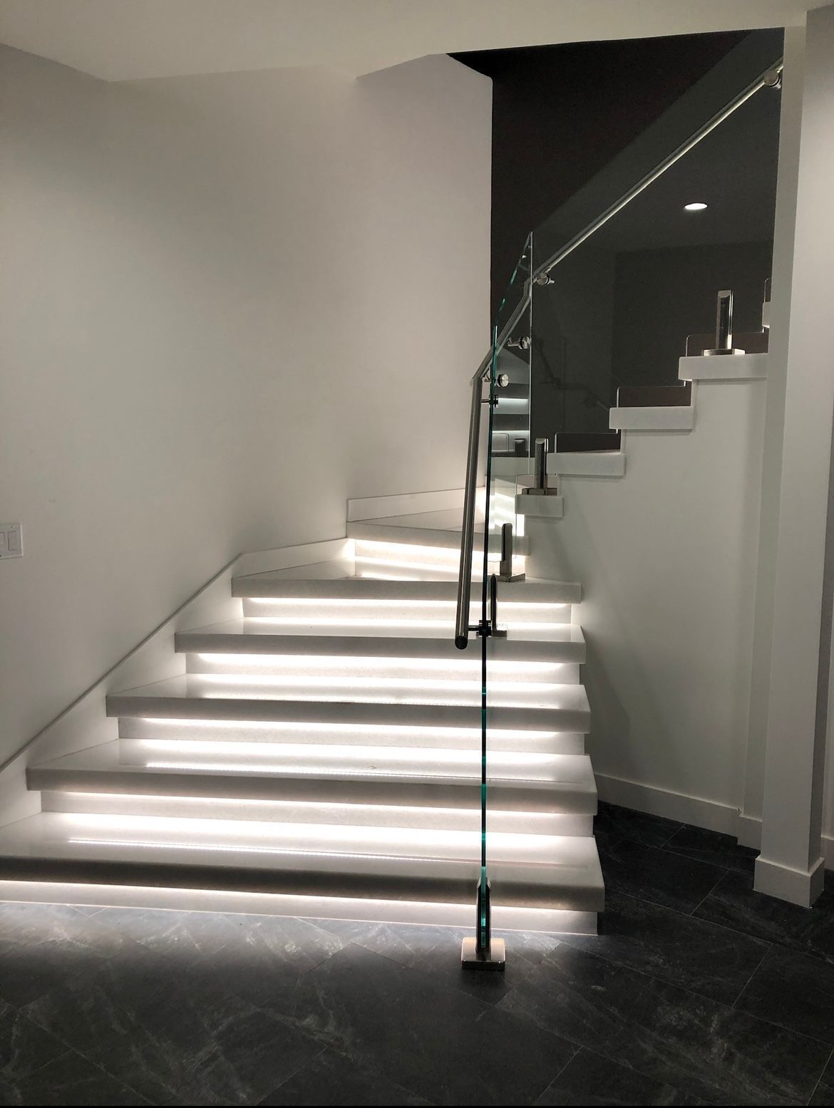 Modern staircase with illuminated steps and glass railing.