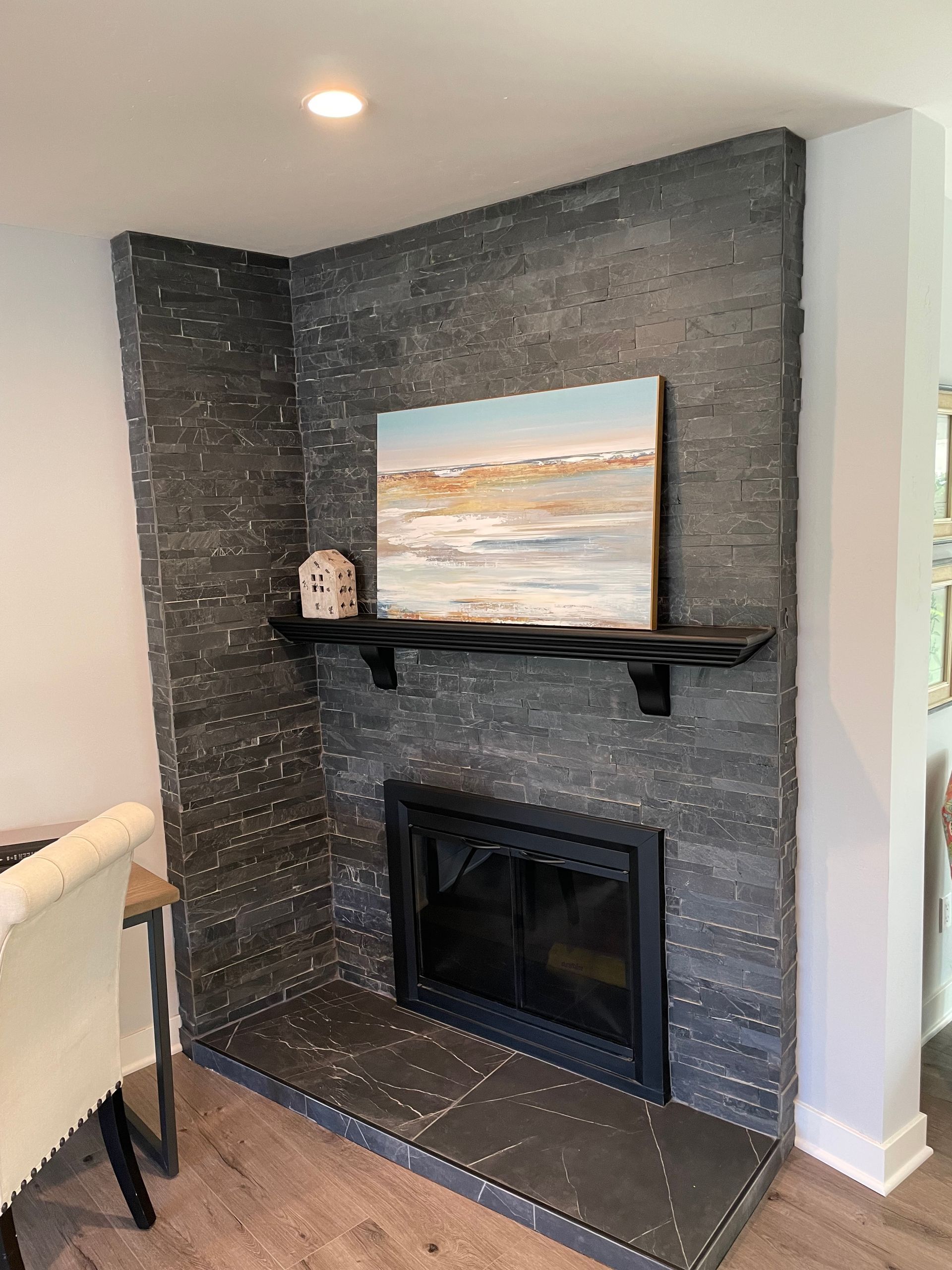 Corner fireplace with dark stone surround, black hearth, and shelf holding art and a small house.