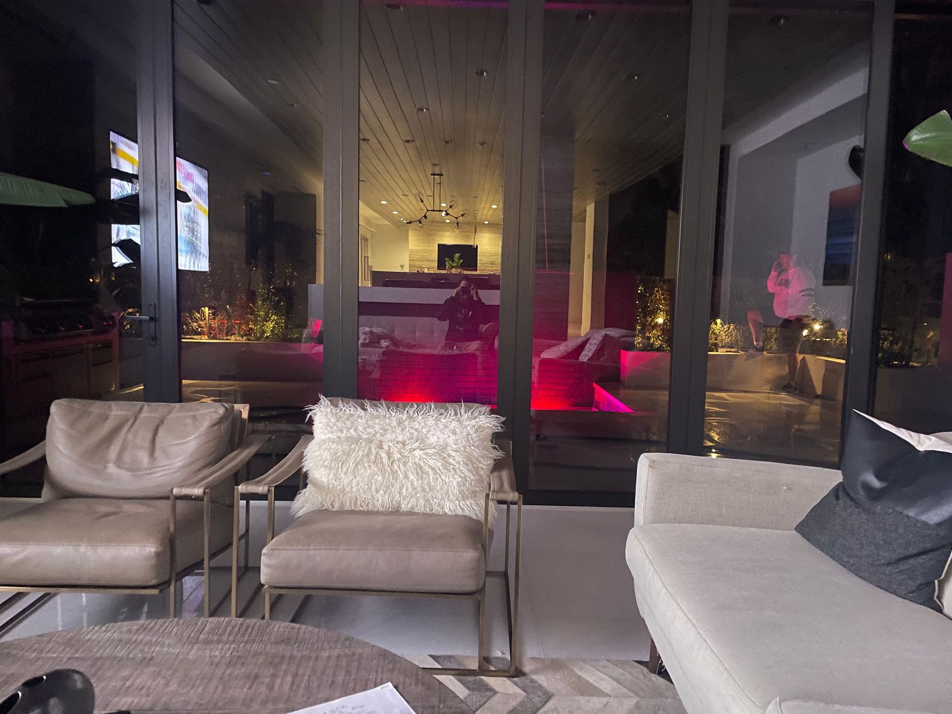 Modern living room with outdoor view at night, lit with pink and warm lights; seating area.