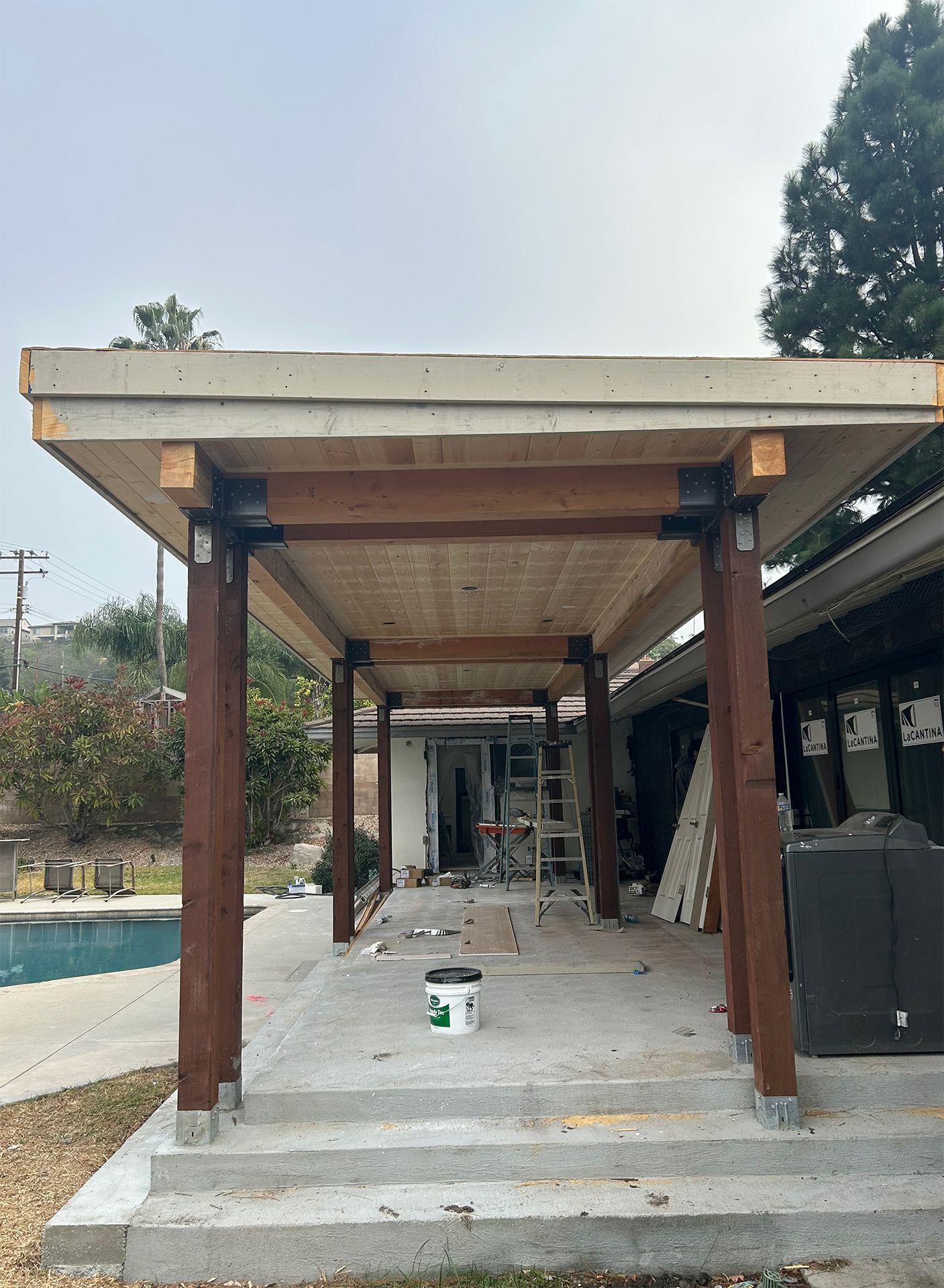 A wooden pergola is being built on the side of a house next to a pool