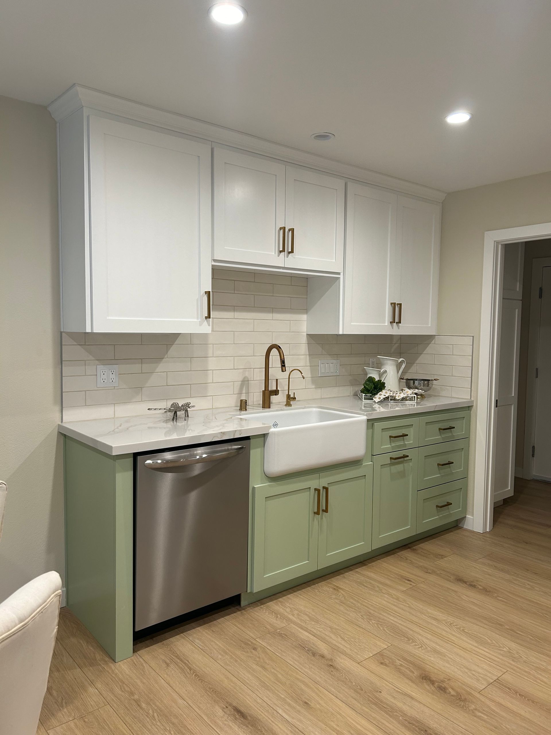 A kitchen with green cabinets , white cabinets , a sink , and a stainless steel dishwasher.