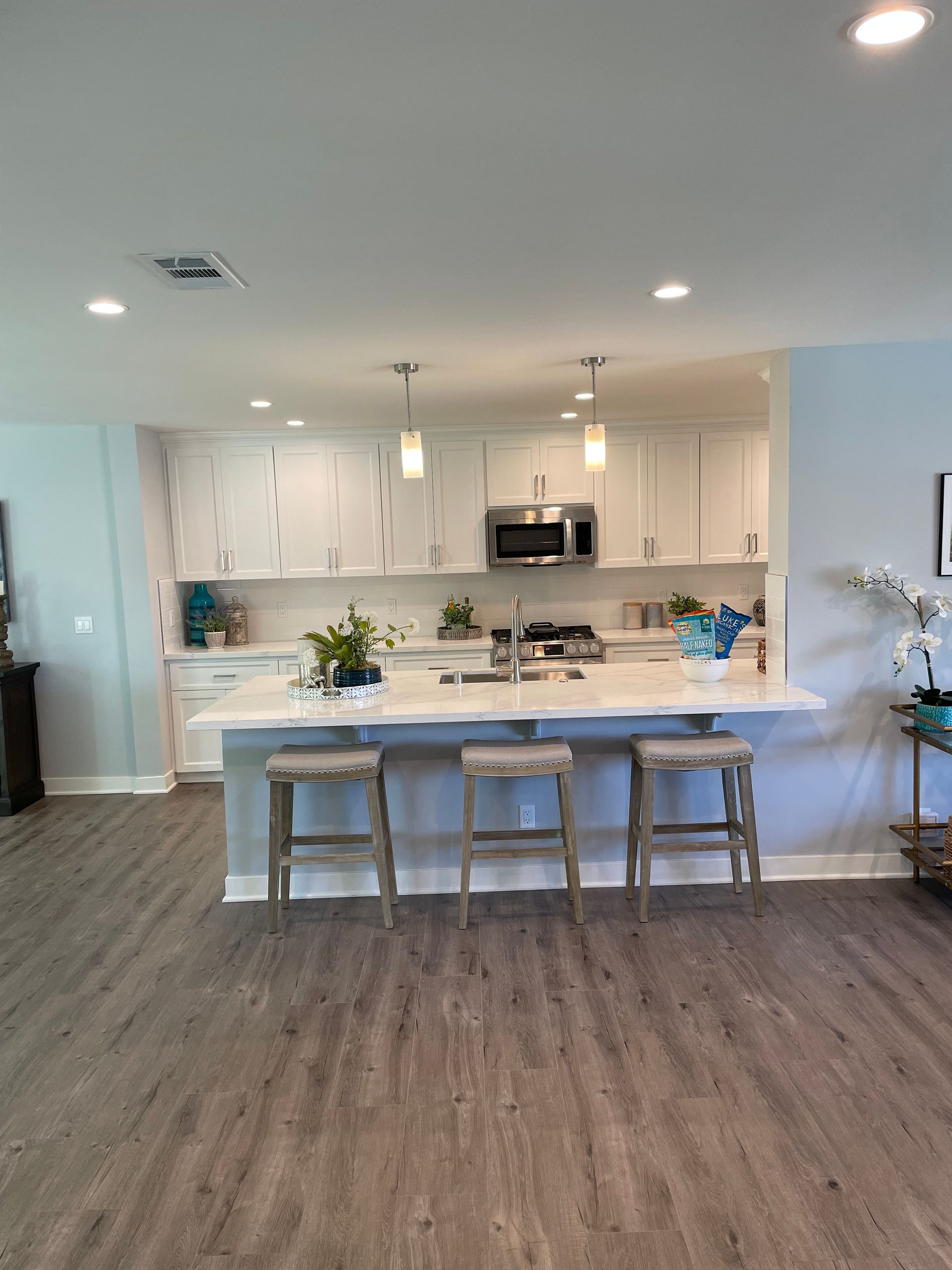 A kitchen with white cabinets and stools and a large island.