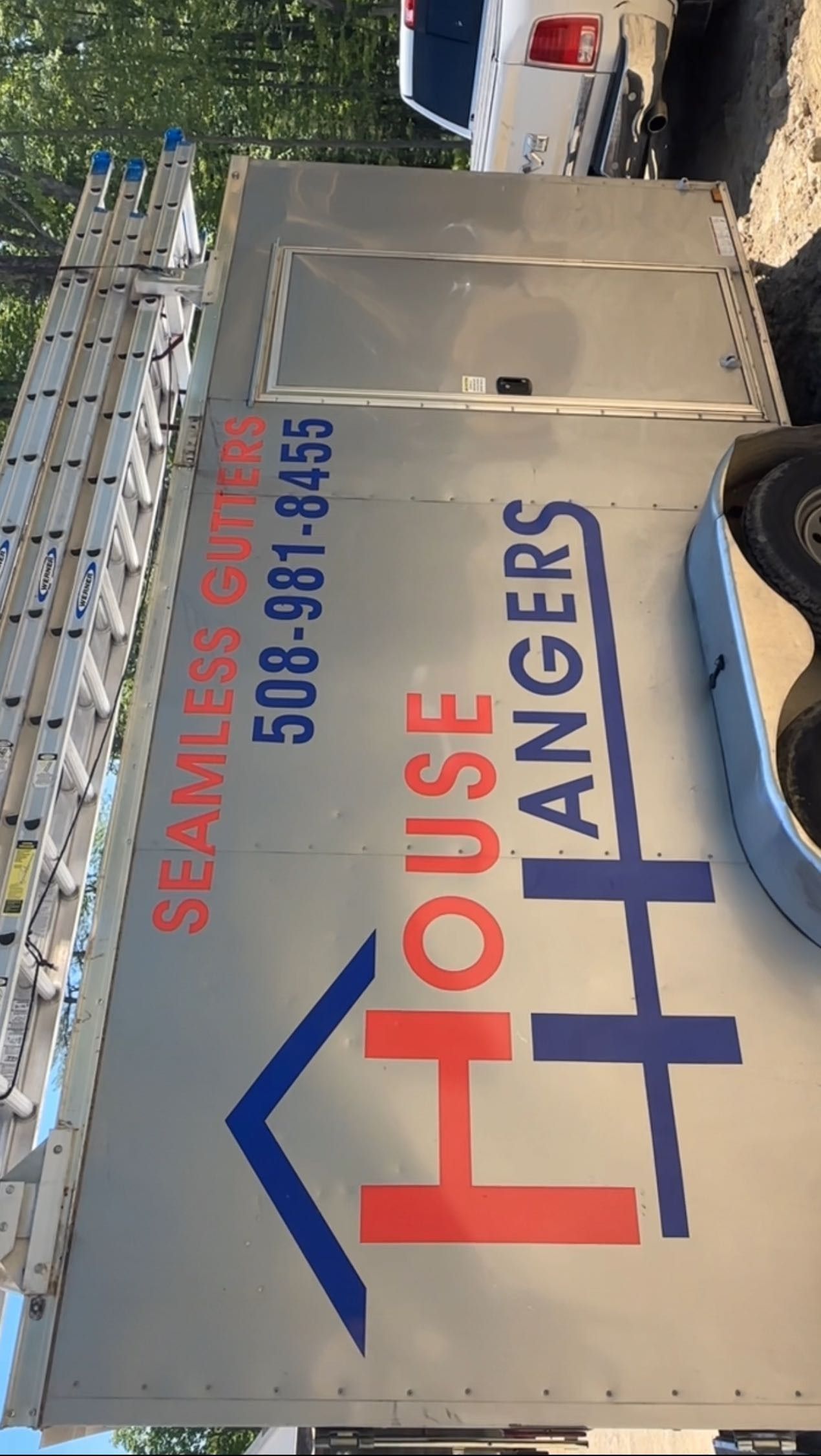 A silver work trailer with blue and red lettering that says 