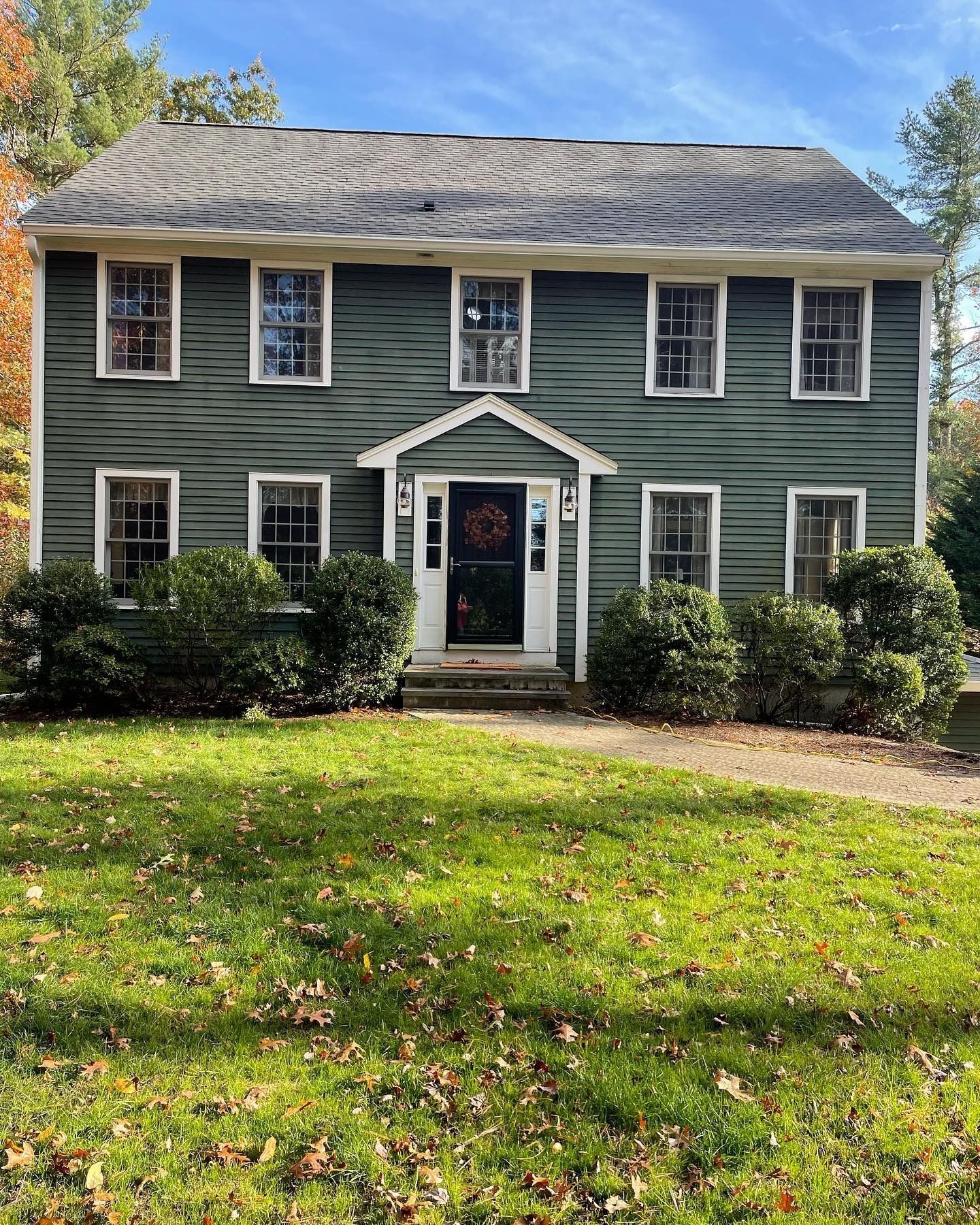 A two-story, dark green colonial house with white trim, a centered front door, and a grassy lawn in the foreground.