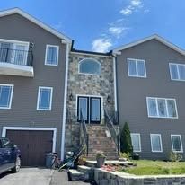A gray two-story house with a central stone entryway, double front doors, a balcony, and a garage under a blue sky.