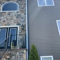 A home exterior with a stone veneer facade, a dark front door, and grey horizontal siding.
