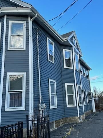 A side view of a two-story blue house with white trim, multiple windows, and a metal utility pole against a blue sky.