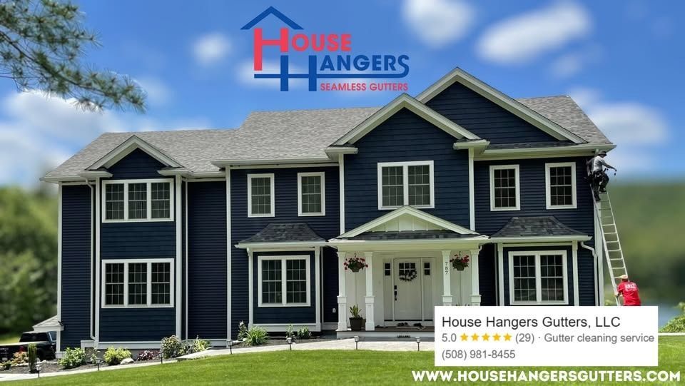 A two-story navy blue house with a white trim, featuring a worker on a ladder installing seamless gutters.