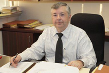 Man in a striped shirt and tie sits at a desk, looking at paperwork, in an office.