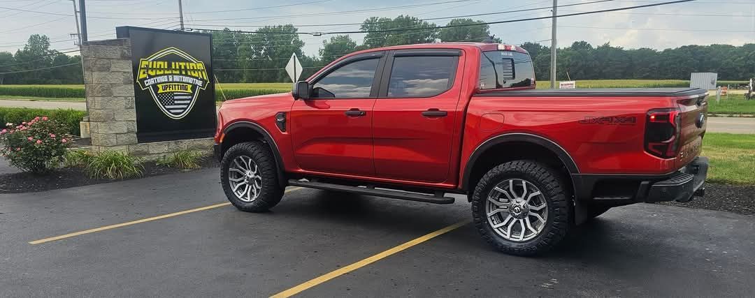 A red truck is parked in a parking lot in front of a sign.