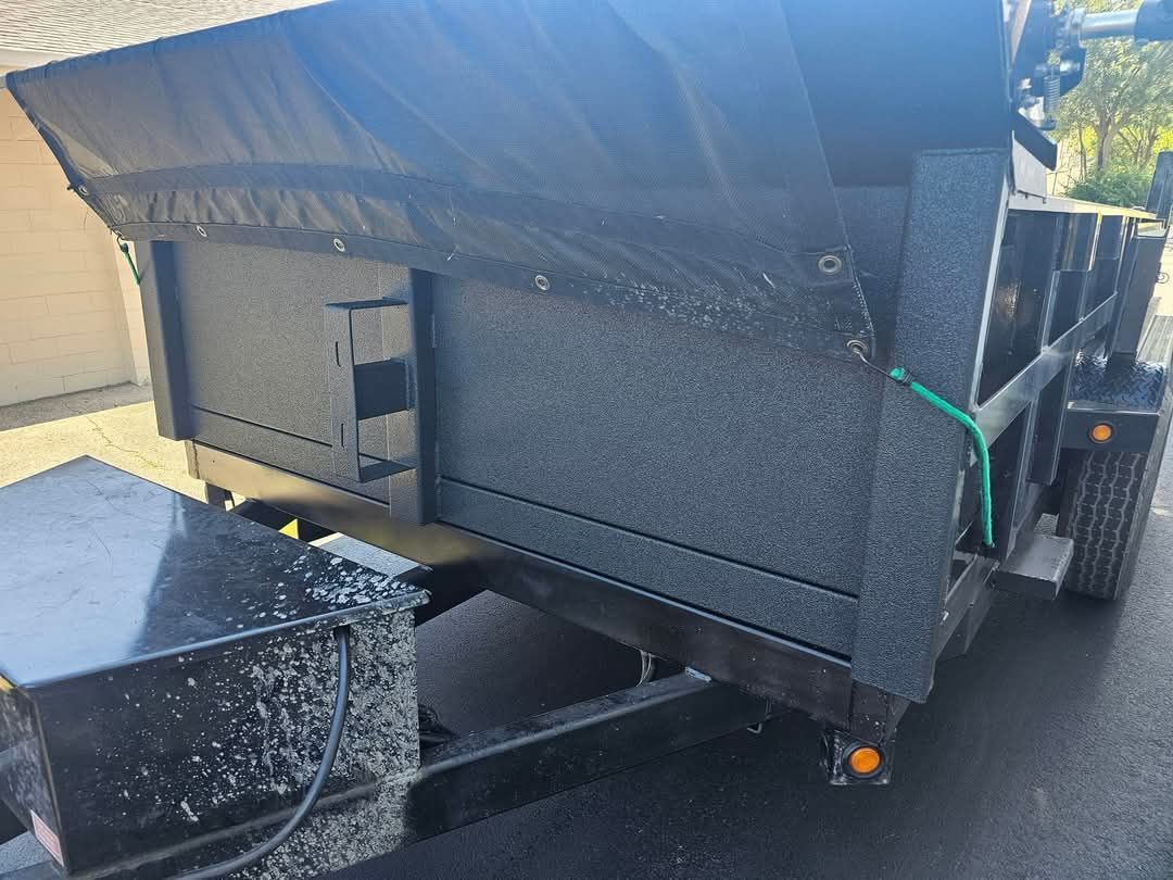 A black dump trailer is parked on the side of the road.