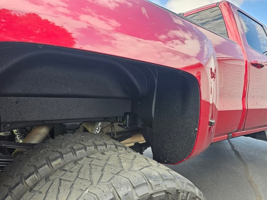 A red truck with big tires is parked on the side of the road.