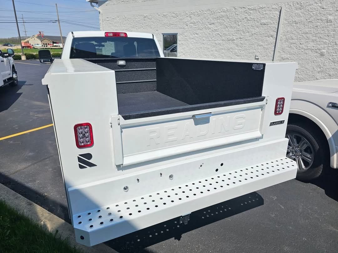 A white truck with a black bed is parked in a parking lot.