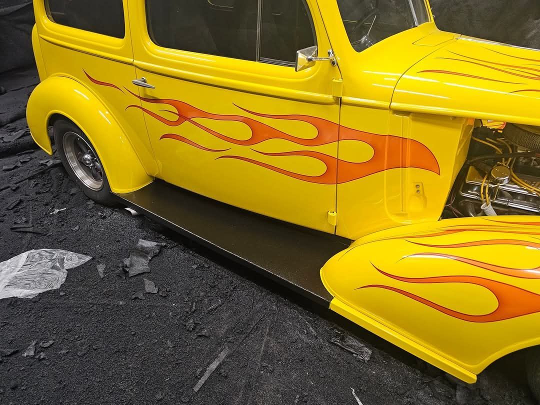 A yellow car with red flames on the side is sitting on the ground.
