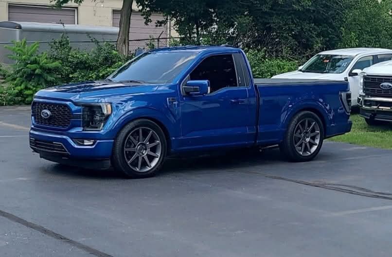 A blue pickup truck is parked in a driveway next to a white truck.