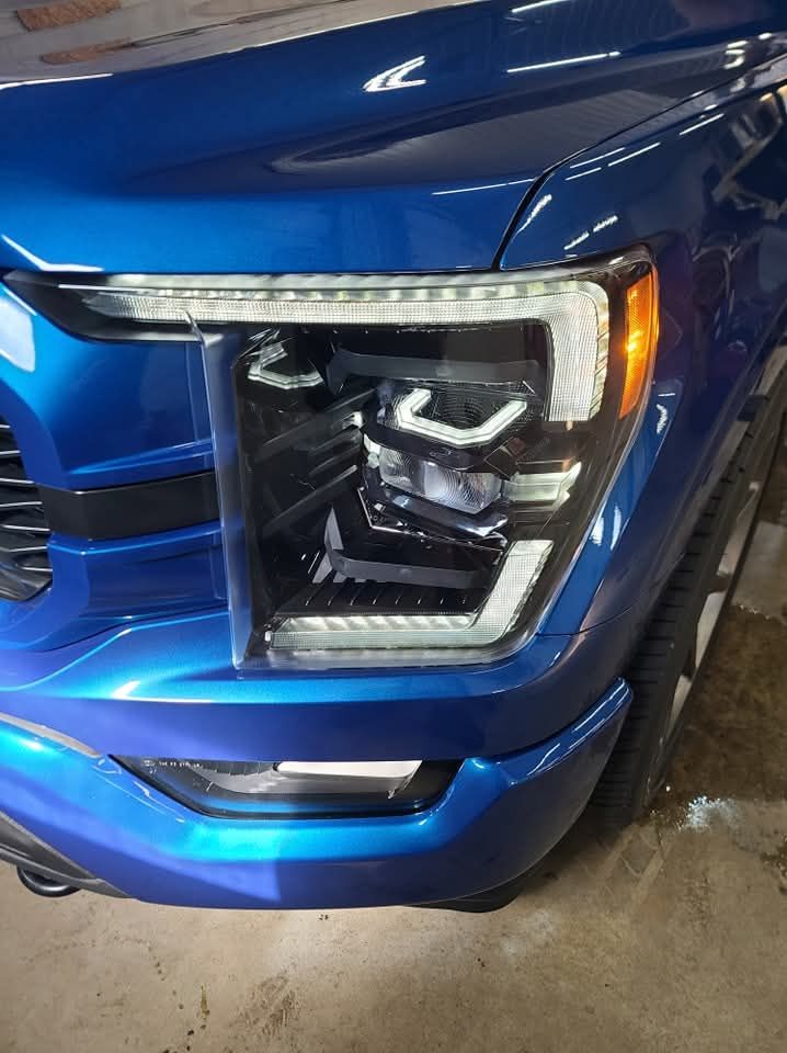 A blue truck with a black headlight is parked in a garage.