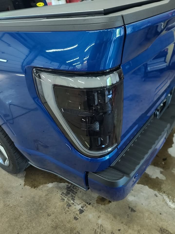 A blue truck with a black tail light is parked in a garage.