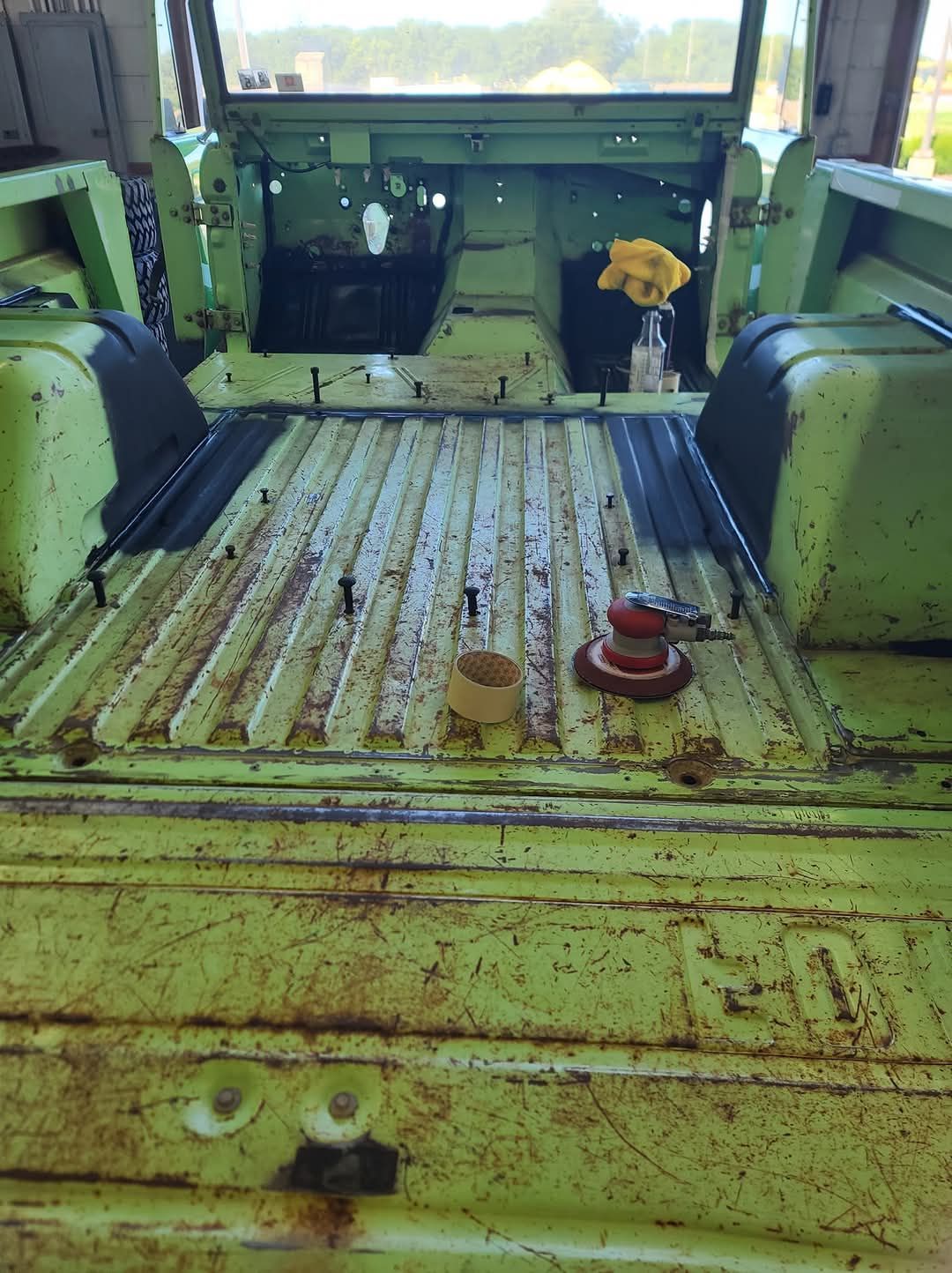 The back of a green truck with a yellow flower in a vase.