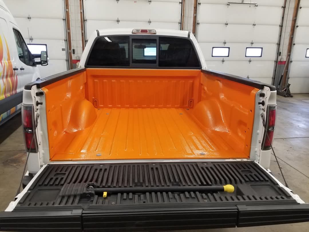 A white truck with an orange bed is parked in a garage.