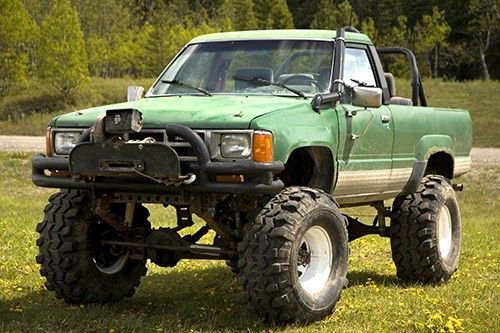 A green truck with big tires is parked in a grassy field.