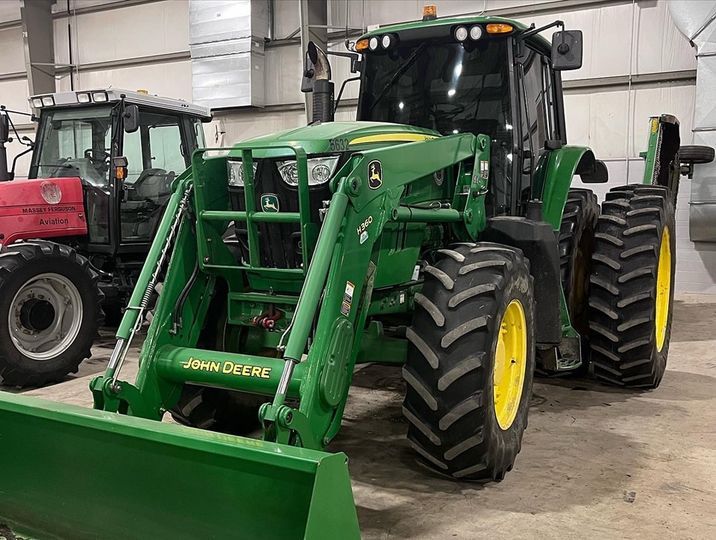 A green john deere tractor with a front loader is parked in a garage.
